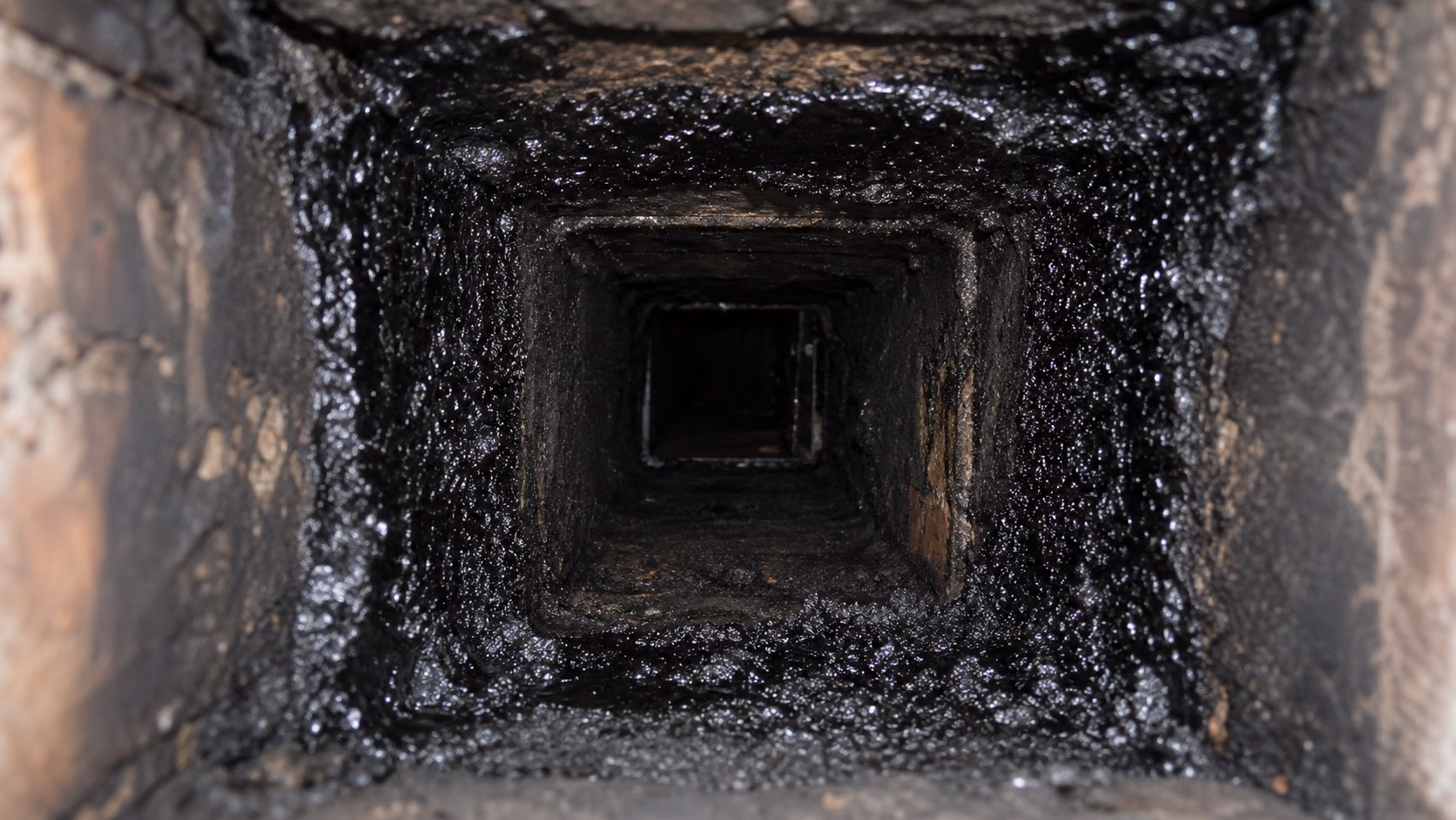 Gros plan sur la paroi intérieure d'un conduit de fumée recouverte de bistre noir et brillant, signe d'un encrassement avancé